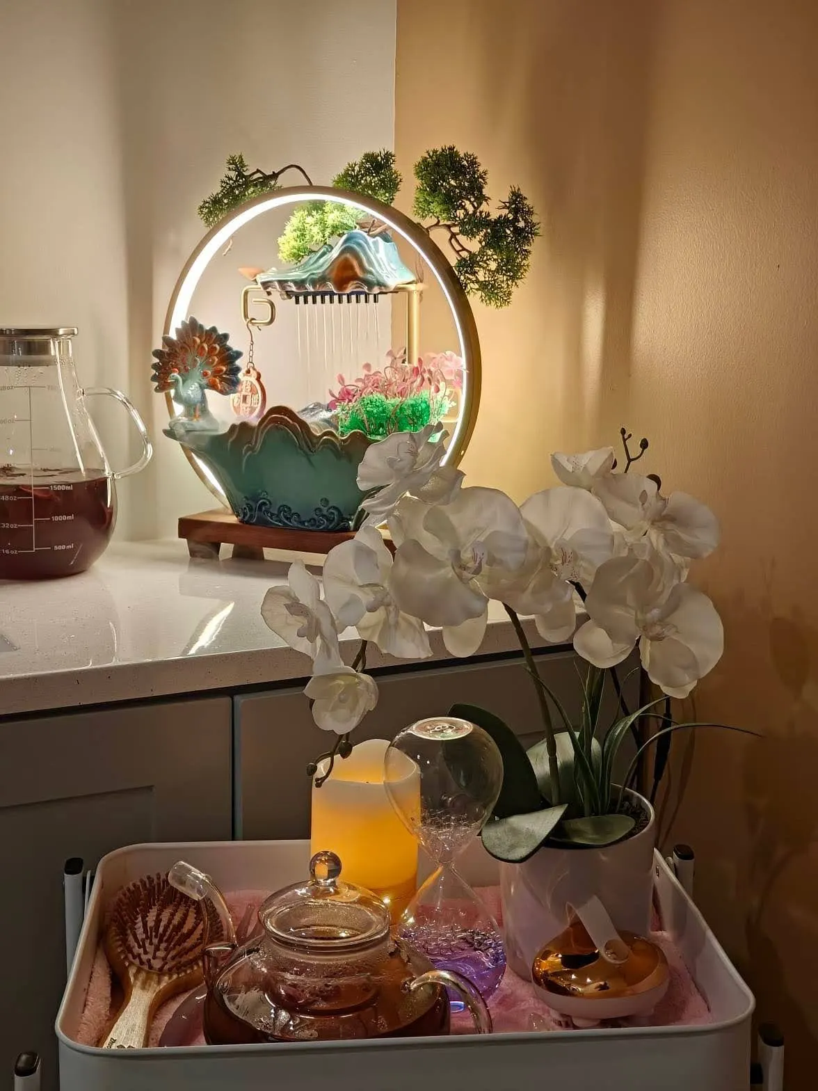 A glass teapot, wooden hairbrush and candle on the tea tray at Fiona's Day Spa in Coon Rapids, MN, beside the lit water feature